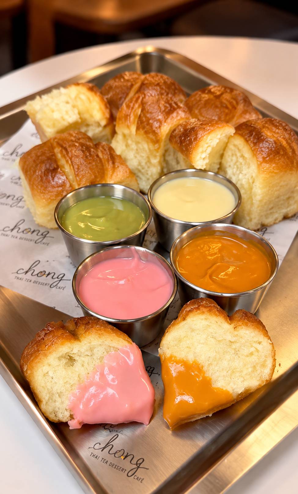 Steamed bread pieces on a steel tray with four dipping cups: green, cream, pink and orange custards.