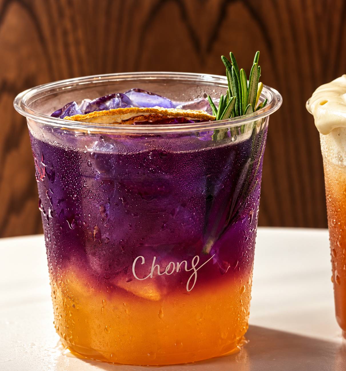 Layered purple and orange iced drink with a dried citrus slice and rosemary sprig.