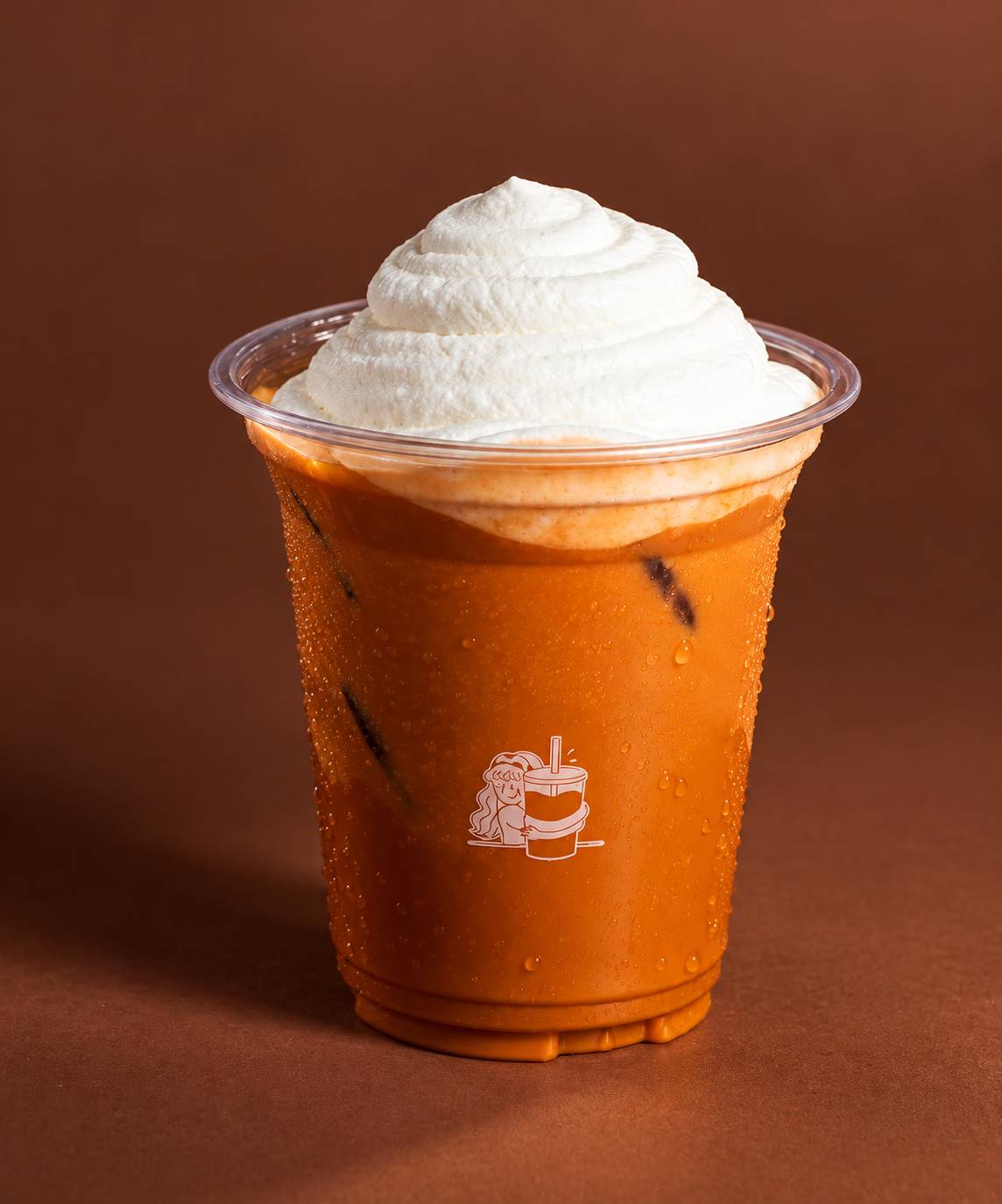 Orange iced tea topped with a swirl of whipped cream, in a clear cup with a line-drawn cup logo.